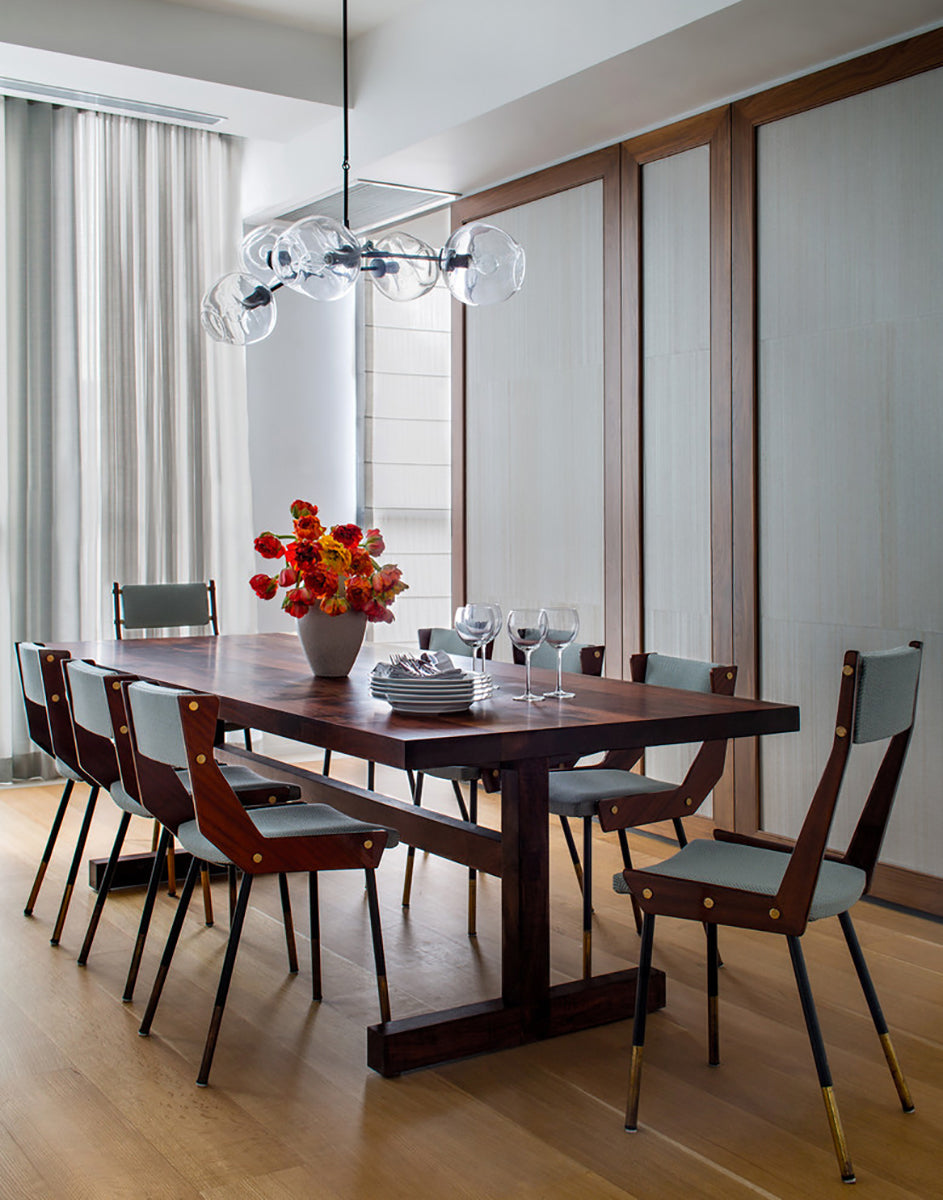 This Clérachic chandelier hangs in a tall room with pale curtains, over a dark wood dining table and slim-legged chairs.