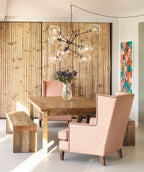 A Clérachic chandelier with clear globes and black arms hangs over a rustic wooden table, with peach wing chairs and a bamboo wall.