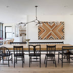 A black-armed Clérachic chandelier extends over a long wooden dining table, with a wooden geometric panel on the wall behind it.