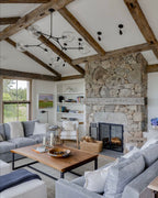This Clérachic chandelier, with black arms and clear globes, hangs under a beamed ceiling above a stone fireplace and a grey sofa.