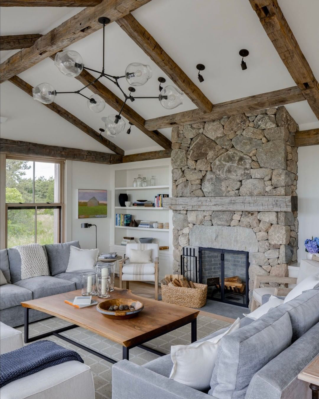 This Clérachic chandelier, with black arms and clear globes, hangs under a beamed ceiling above a stone fireplace and a grey sofa.