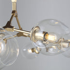 Close view of a clear glass globe and gold branching joint on this Clérachic chandelier, with the bulb visible inside.