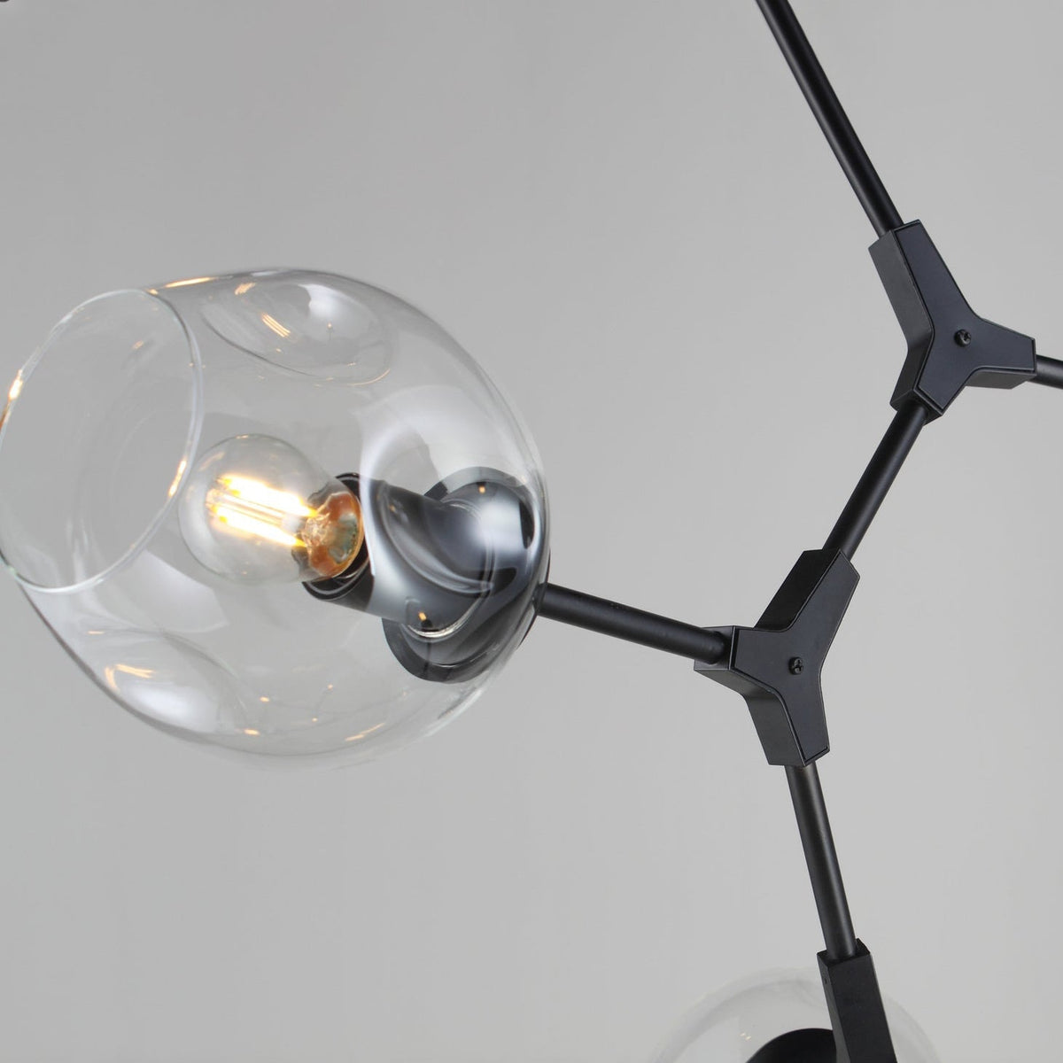 Close view of a dimpled clear glass globe on a black arm and Y-shaped joint of this Clérachic chandelier.