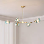 Gold Clérachic chandelier with five gradient blue glass globes lit softly, hung from a slim rod in a pale room with white curtains.