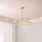 Gold Clérachic chandelier with seven amber glass globes lit on a branching frame, hung below a white ceiling beside pale curtains.