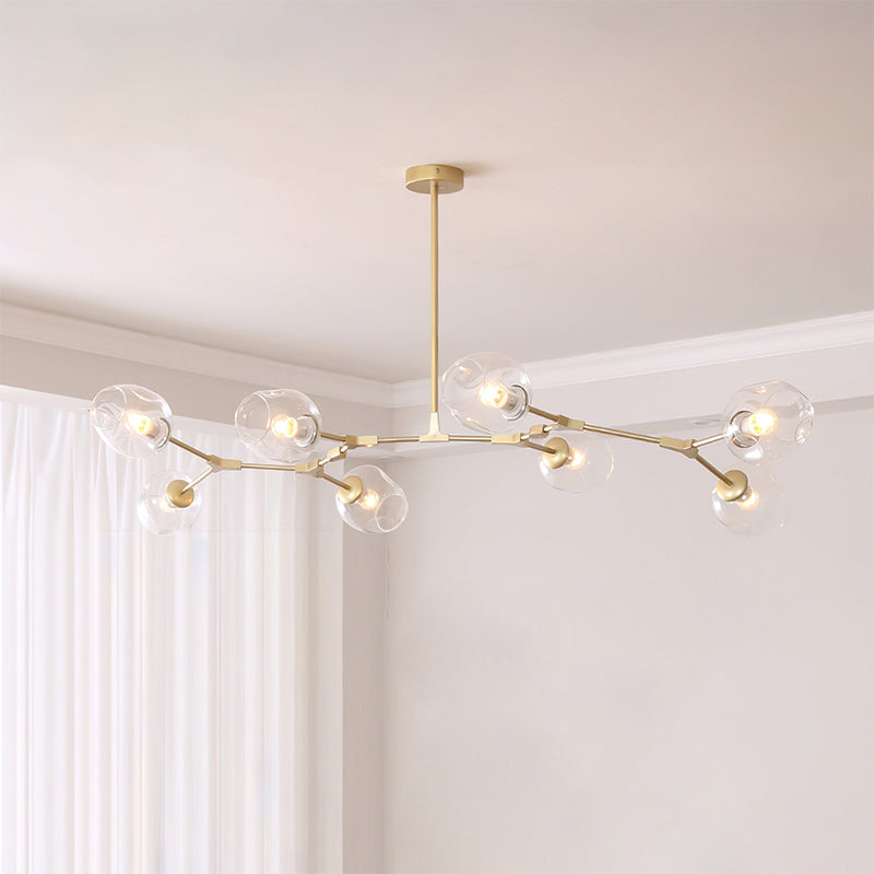 Gold Clérachic chandelier with eight clear glass globes on a branching frame, hung from a rod in a pale corner room.