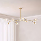 Gold Clérachic chandelier with eight clear glass globes on a branching frame, hung from a rod in a pale corner room.