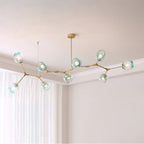 Long gold Clérachic chandelier with nine gradient blue glass globes lit along a branching frame, hung in a pale corner room.