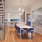 A Clérachic chandelier with brass-toned arms and clear glass globes above a white dining table, in an open kitchen beside a staircase.