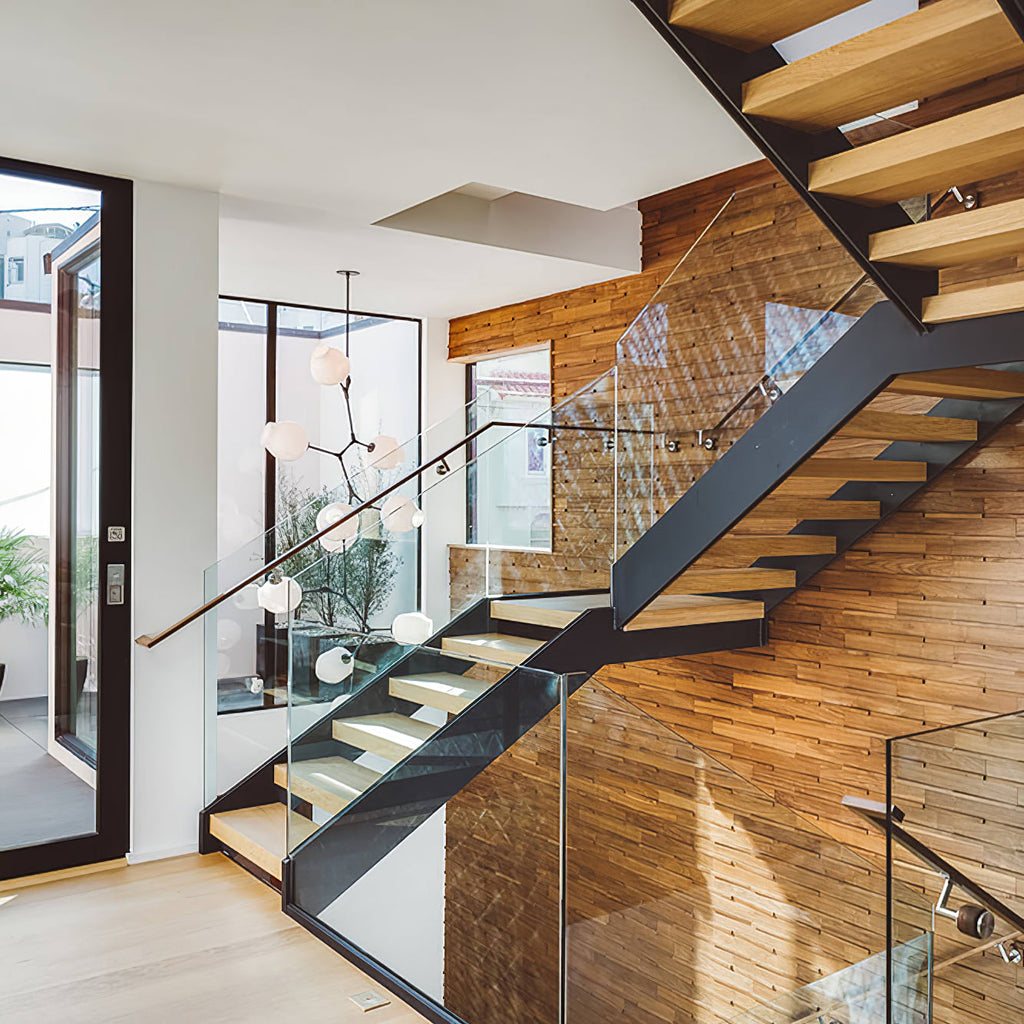 Clérachic glass-globe chandelier hanging in a stairwell with open timber treads, a glass balustrade and a wood-clad wall.