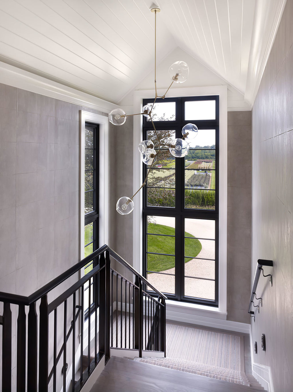 Tall Clérachic chandelier dropping through a stairwell with a black-framed window, a white panelled ceiling and a black balustrade.