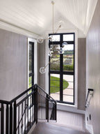 Tall Clérachic chandelier dropping through a stairwell with a black-framed window, a white panelled ceiling and a black balustrade.