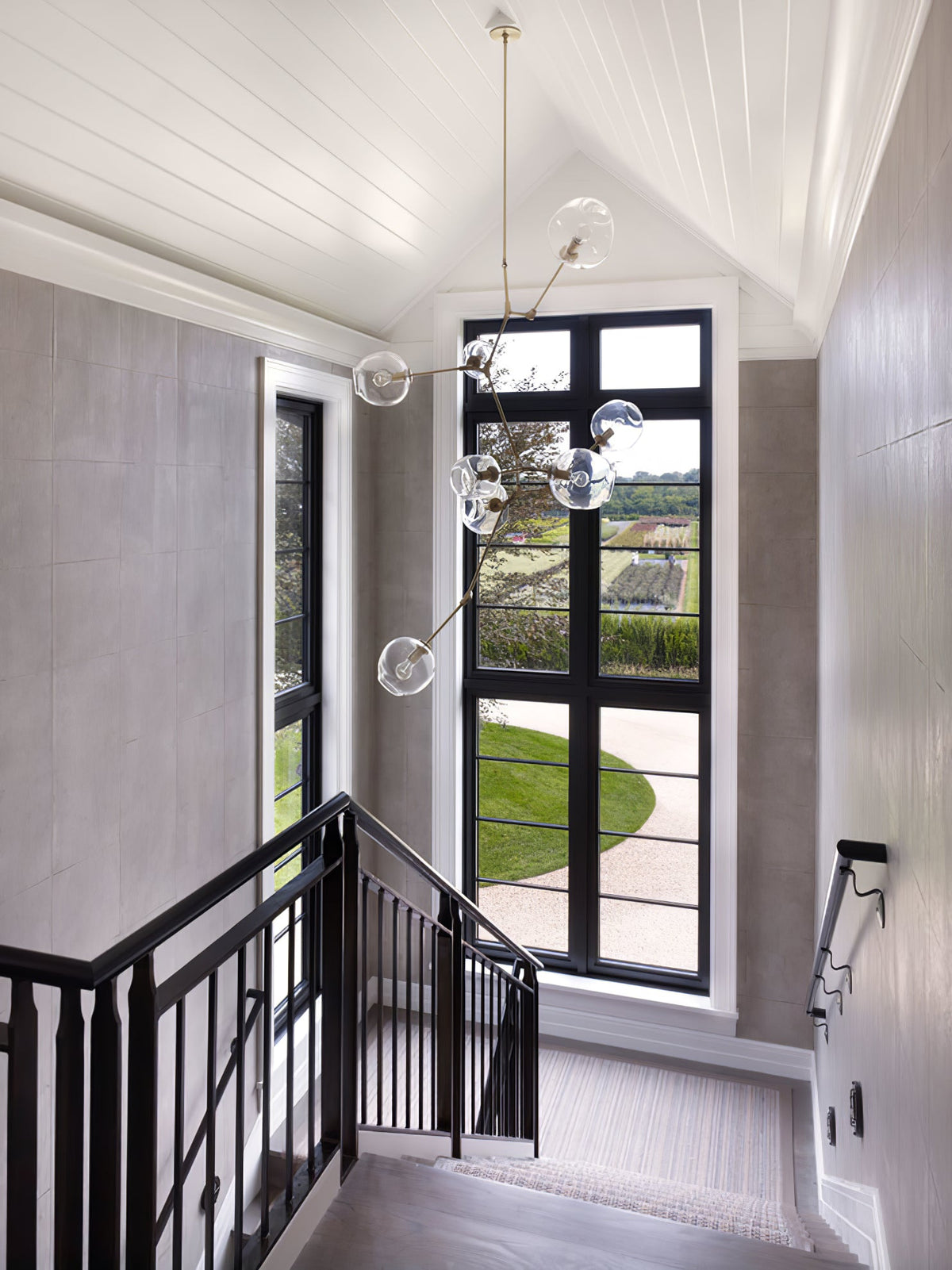 Tall Clérachic chandelier dropping through a stairwell with a black-framed window, a white panelled ceiling and a black balustrade.