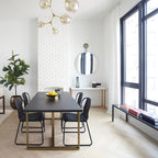 Clérachic chandelier with gold arms and amber glass globes in a tall dining room with a white brick chimney breast and black windows.