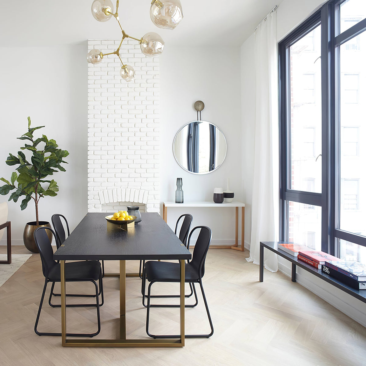 Clérachic chandelier with gold arms and amber glass globes in a tall dining room with a white brick chimney breast and black windows.