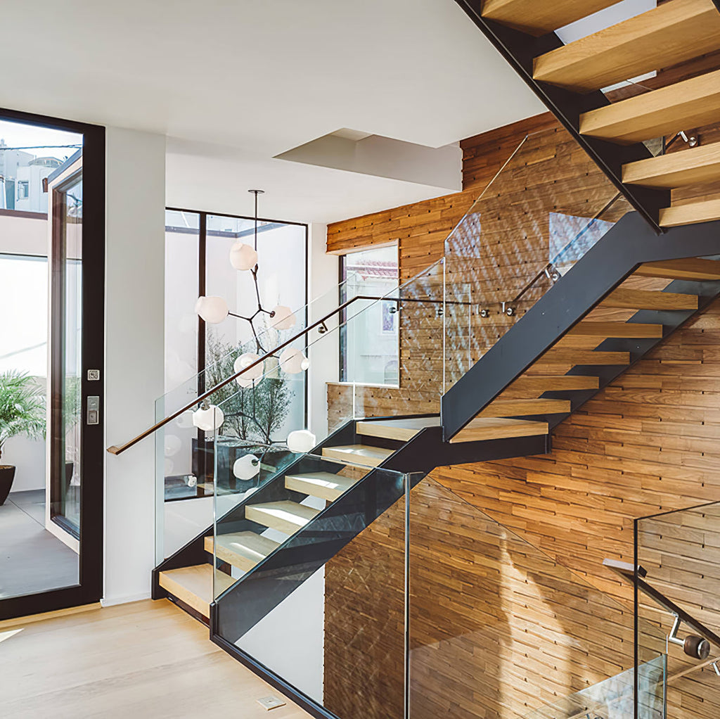 Wider view of the Clérachic chandelier over a stairwell with timber treads, glass panels and a wood-clad wall.
