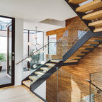 Wider view of the Clérachic chandelier over a stairwell with timber treads, glass panels and a wood-clad wall.