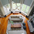 Looking down on a living room from above, with a Clérachic chandelier of brass arms and clear globes hanging by a bay window.