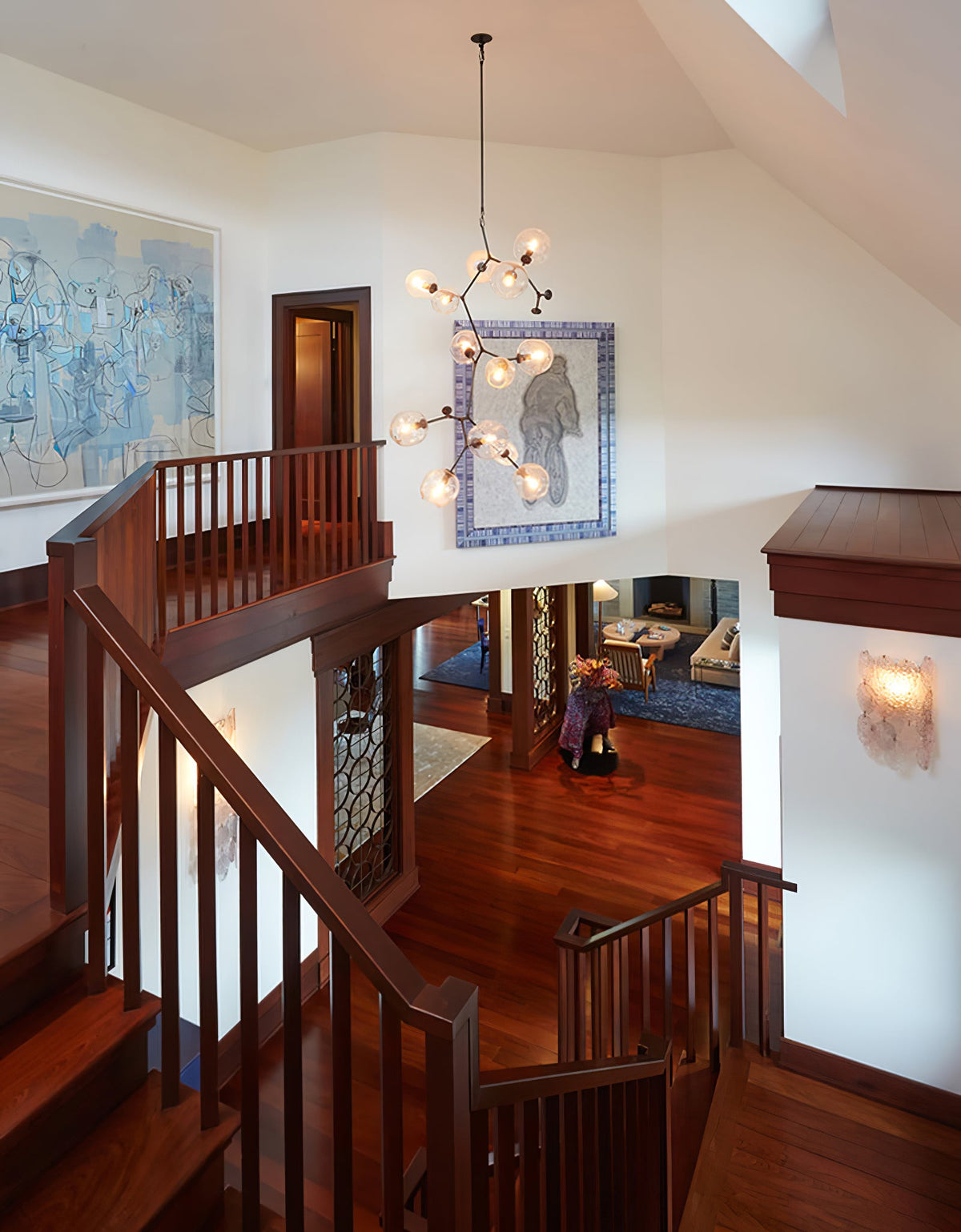Clérachic chandelier in a stairwell above a polished wooden staircase, with blue artwork on the wall behind it.