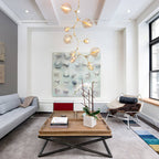 A tall Clérachic chandelier with gold-toned arms and clear globes rising in a loft living room above a square coffee table.