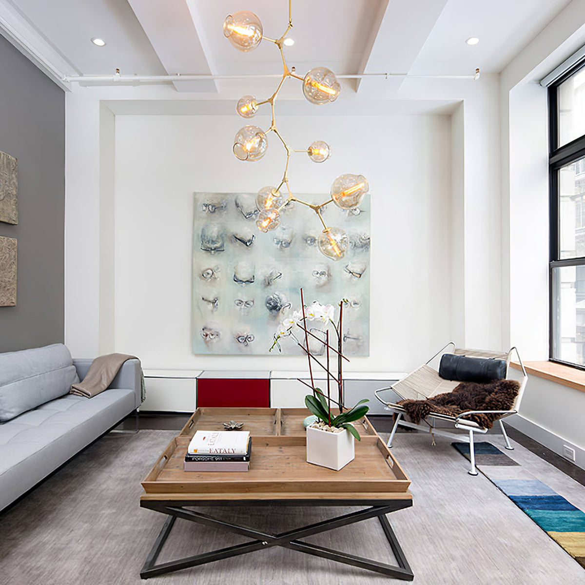 A tall Clérachic chandelier with gold-toned arms and clear globes rising in a loft living room above a square coffee table.