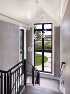 Clérachic chandelier with clear globes hanging through a stairwell beside a tall black-framed window and a black balustrade.