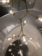 Looking down a spiral stair, with a lit Clérachic chandelier in brass and clear globes branching out in the foreground.