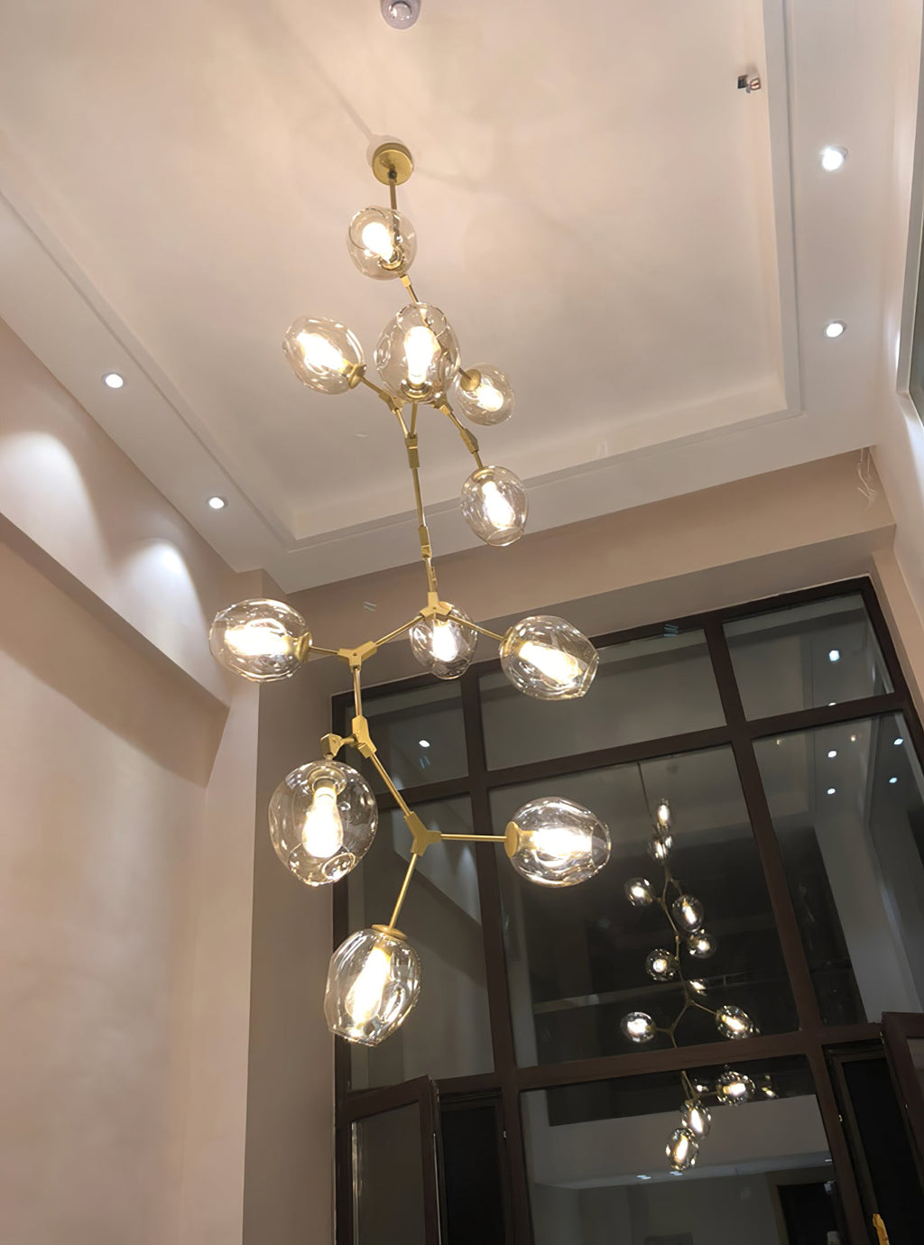 Lit Clérachic chandelier with clear globes rising through a tall stairwell with a coffered ceiling and a glazed screen.