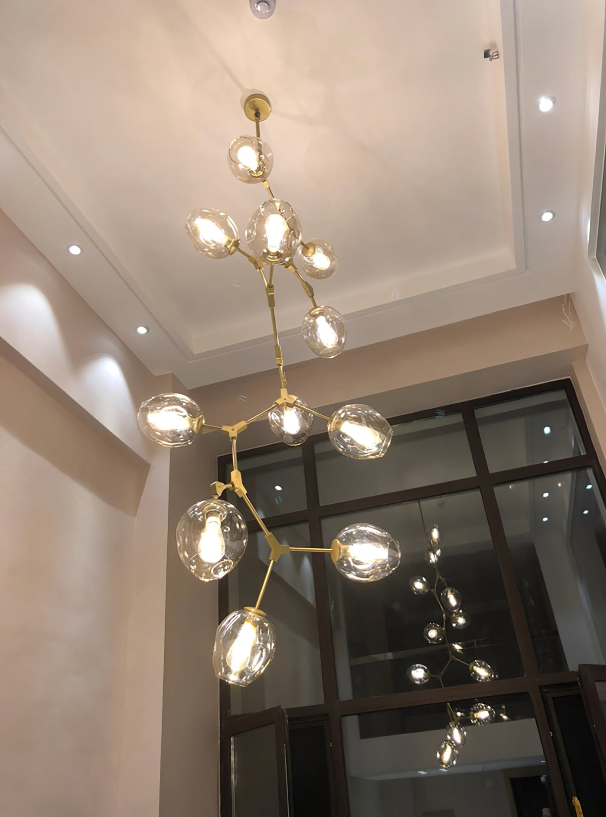 Lit Clérachic chandelier with clear globes rising through a tall stairwell with a coffered ceiling and a glazed screen.