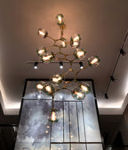 Lit Clérachic chandelier in brass with clear globes hanging in a double-height space above track lights and a glazed wall.