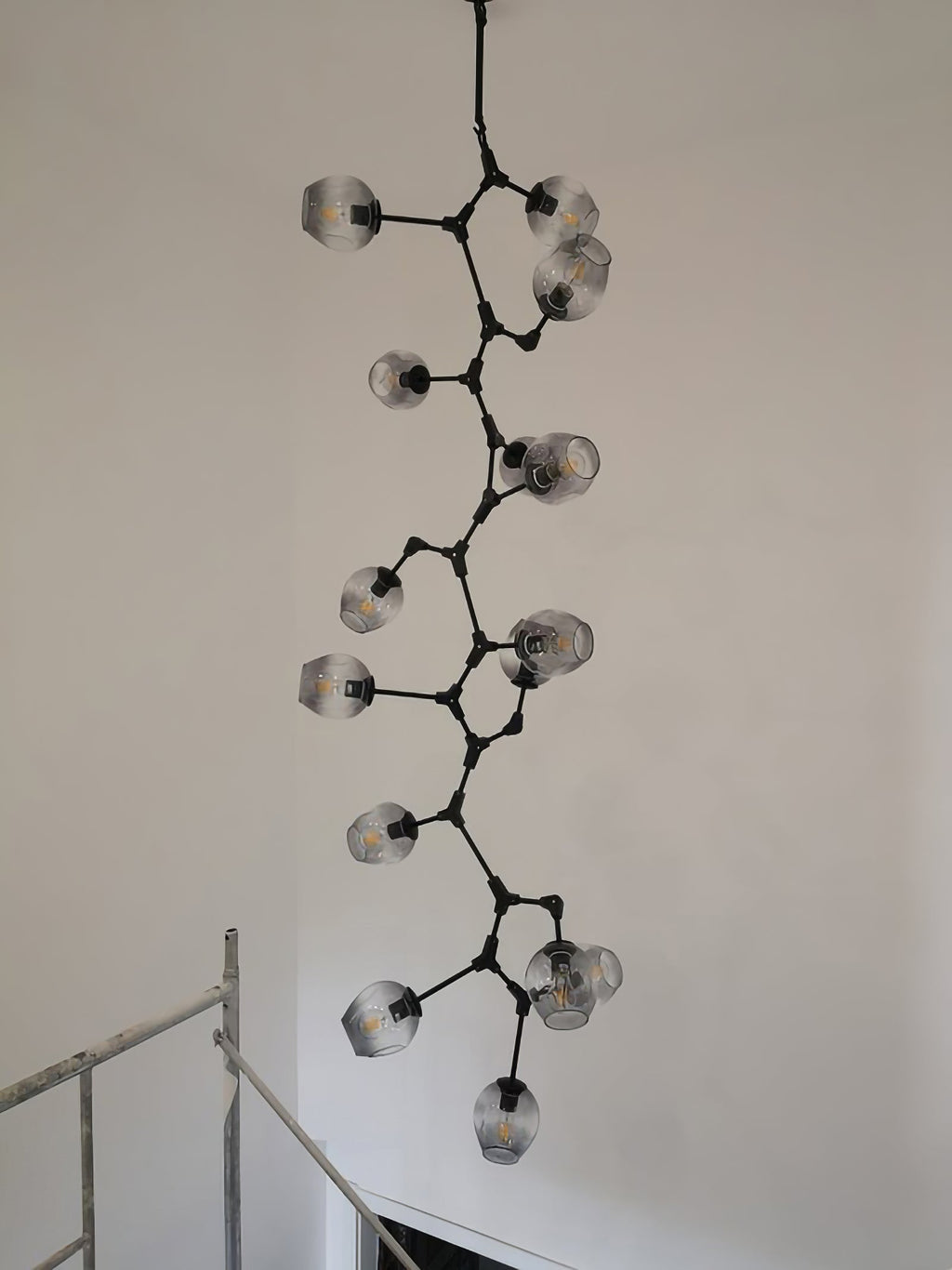 A very long black-framed Clérachic chandelier with smoky grey globes running down a tall stairwell wall.
