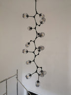 A very long black-framed Clérachic chandelier with smoky grey globes running down a tall stairwell wall.