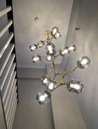 Looking up at a lit Clérachic chandelier with brass arms and smoky grey globes in a narrow stairwell.