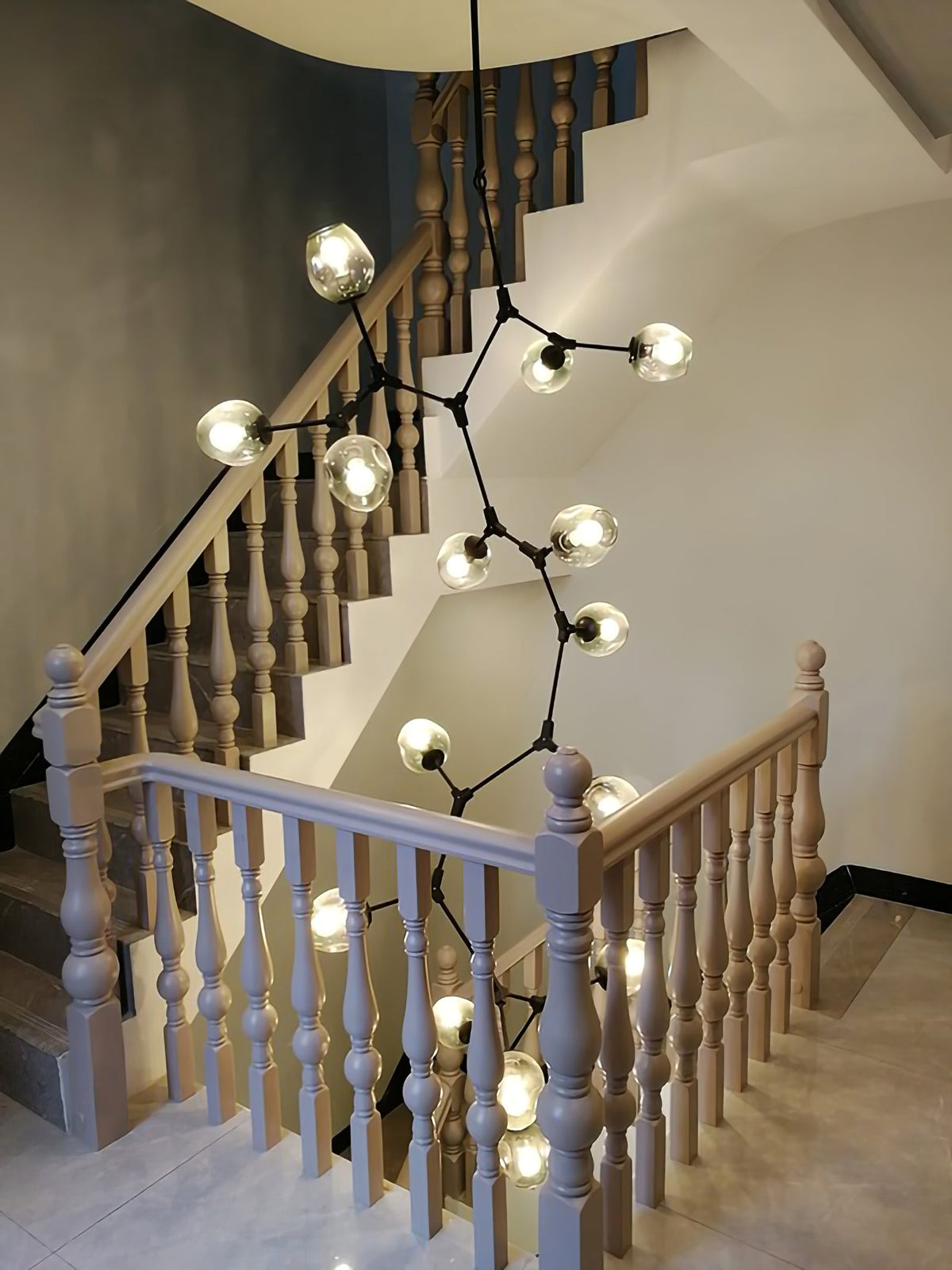 Clérachic chandelier with clear globes and thin black arms winding down through a stairwell with turned wooden balusters.