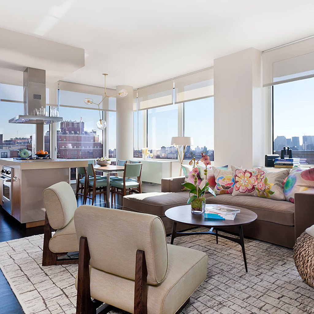 A Clérachic chandelier hanging in a bright open-plan flat with a sofa, two lounge chairs and a city view through the windows.