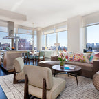 A Clérachic chandelier hanging in a bright open-plan flat with a sofa, two lounge chairs and a city view through the windows.