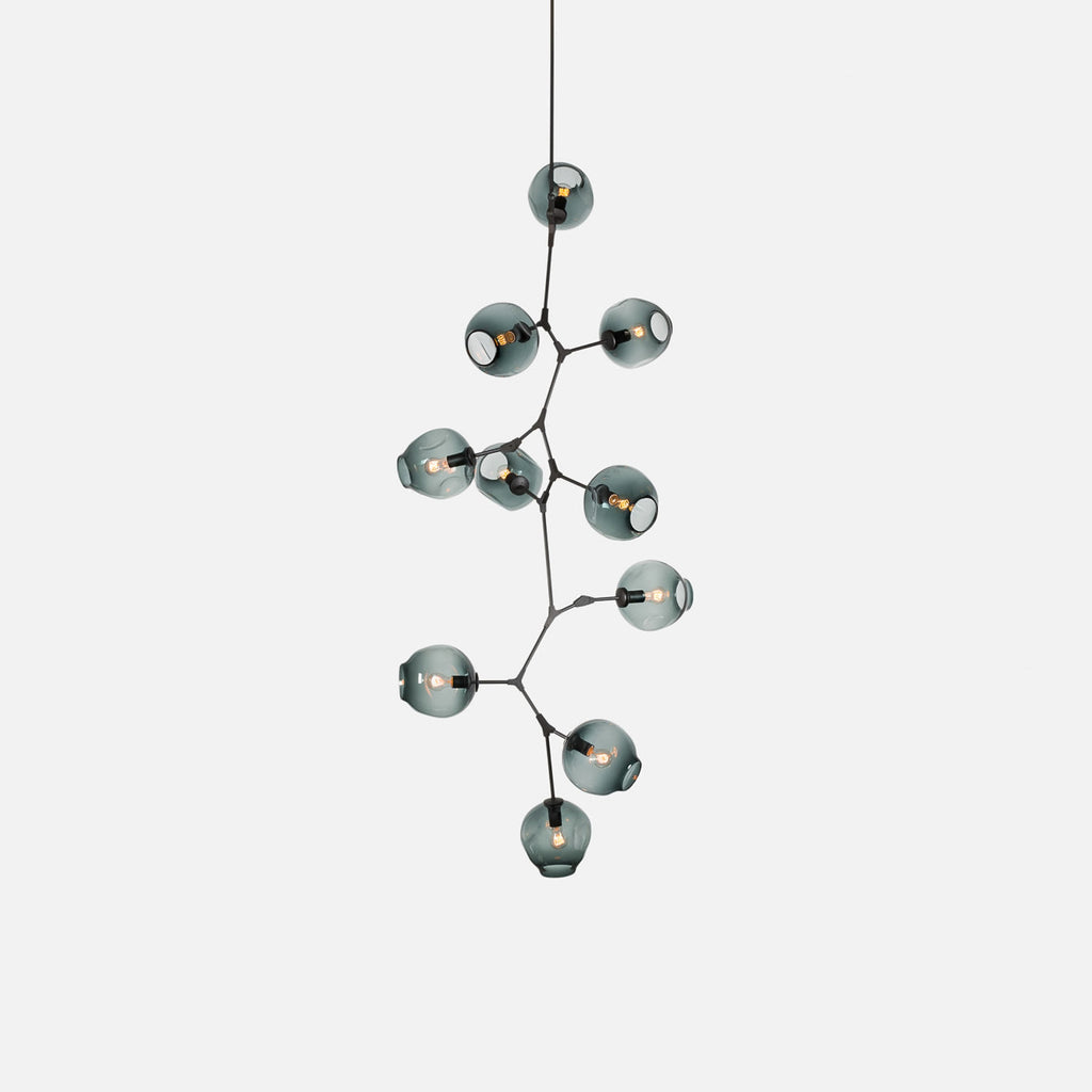 Black-framed Clérachic chandelier on a pale grey backdrop, with smoky blue-grey globes stepping down a branching frame.