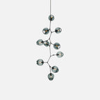 Black-framed Clérachic chandelier on a pale grey backdrop, with smoky blue-grey globes stepping down a branching frame.