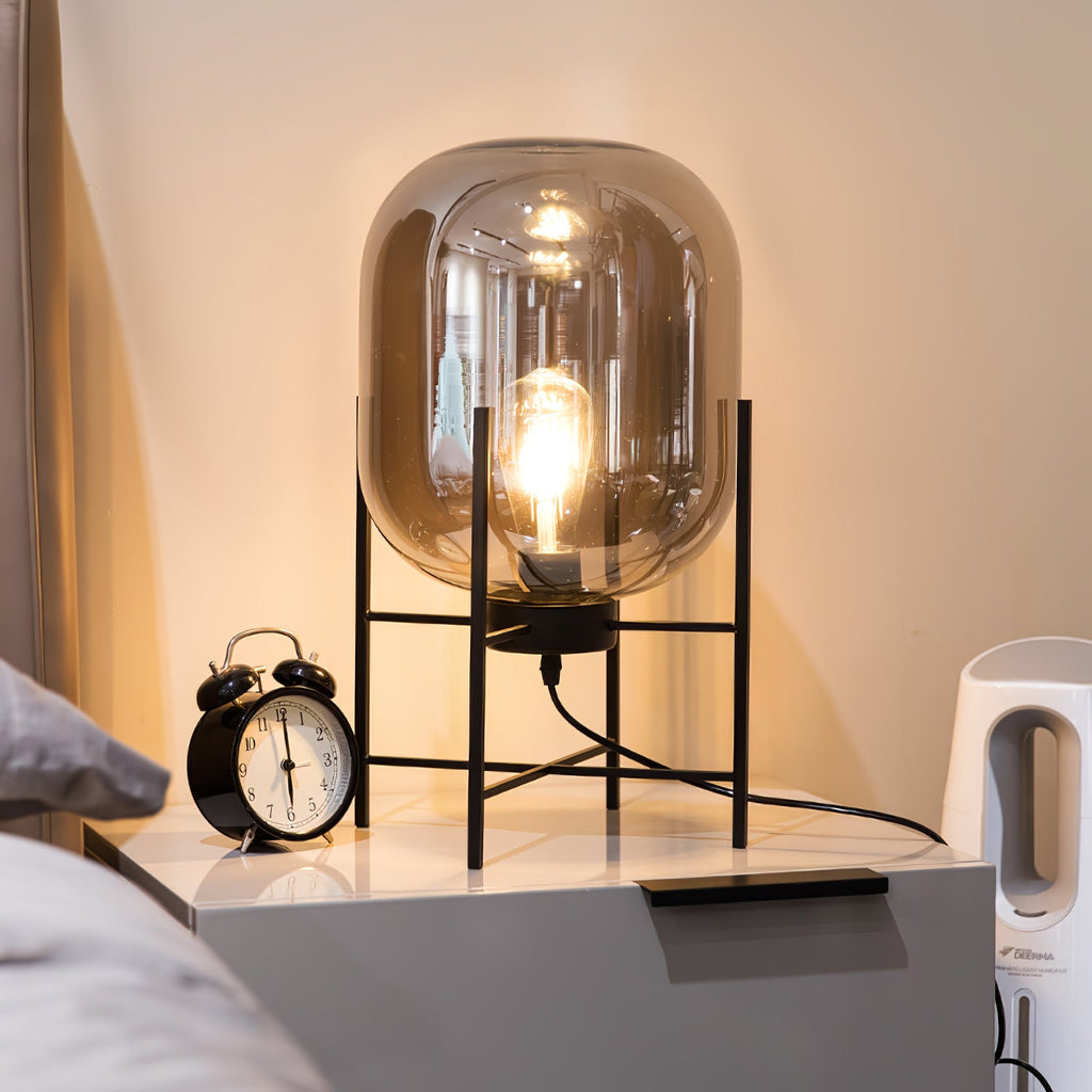 Lit amber glass shade glowing warmly on this Clérachic table lamp, beside an alarm clock on a grey bedside cabinet.