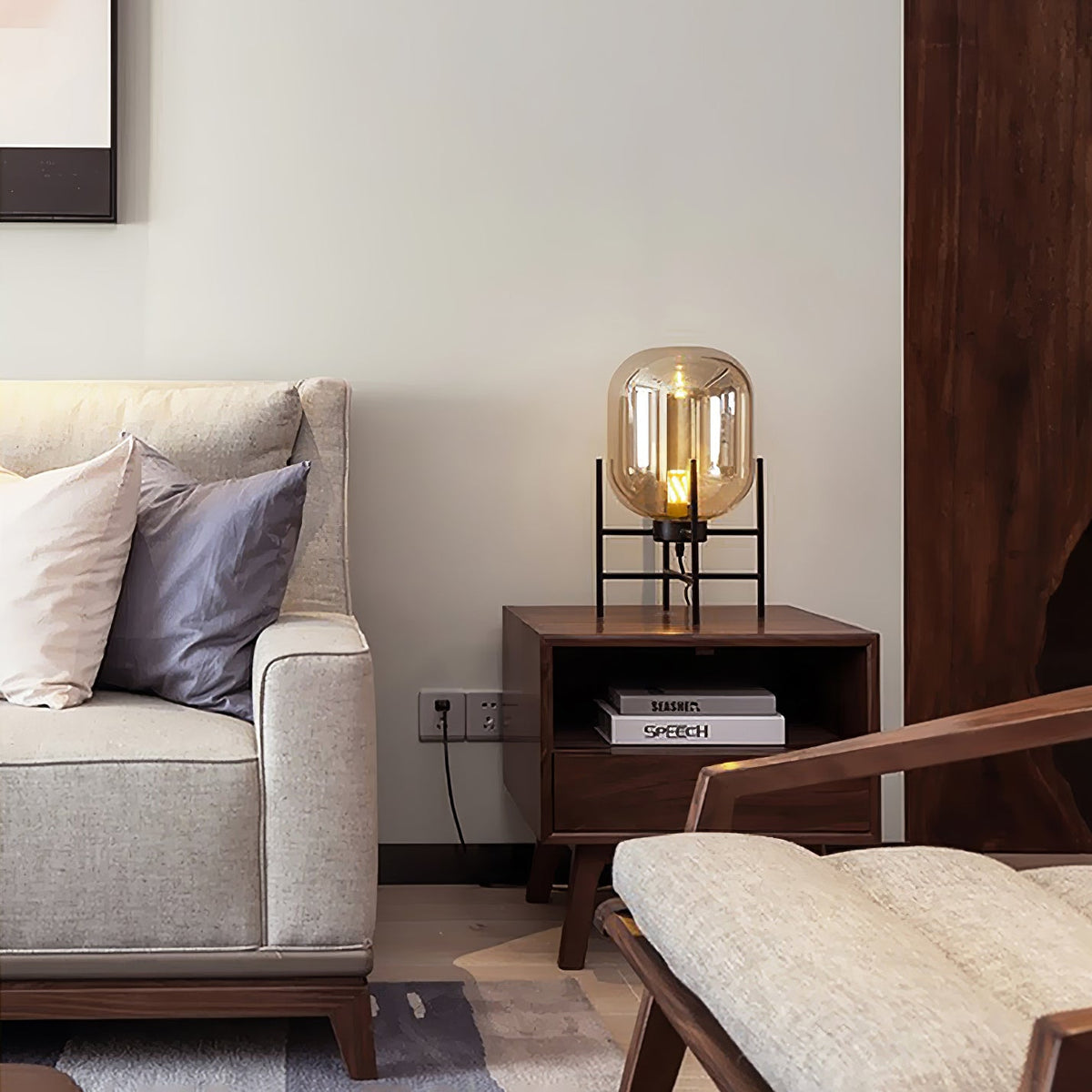Small amber-glass Clérachic lamp on a dark wood side table, set between a cream armchair and a sofa with soft cushions.