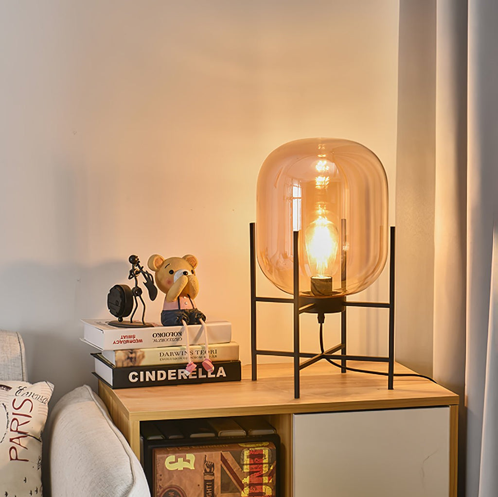 Warm orange-amber glass glows around the bulb in this Clérachic table lamp, standing on a wooden shelf unit with books.