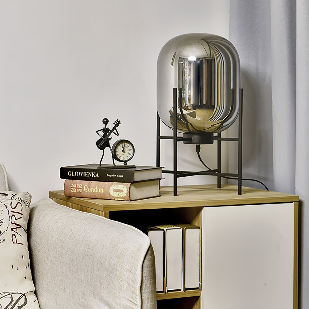 Mirrored smoke-grey glass shade on a black stand, this Clérachic lamp on a shelf beside a clock and a few books.