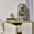 Mirrored smoke-grey glass shade on a black stand, this Clérachic lamp on a shelf beside a clock and a few books.