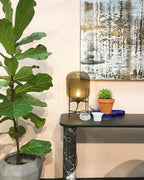 Amber glass lamp from Clérachic on a dark console table, beside a potted succulent and a tall green fiddle-leaf plant.