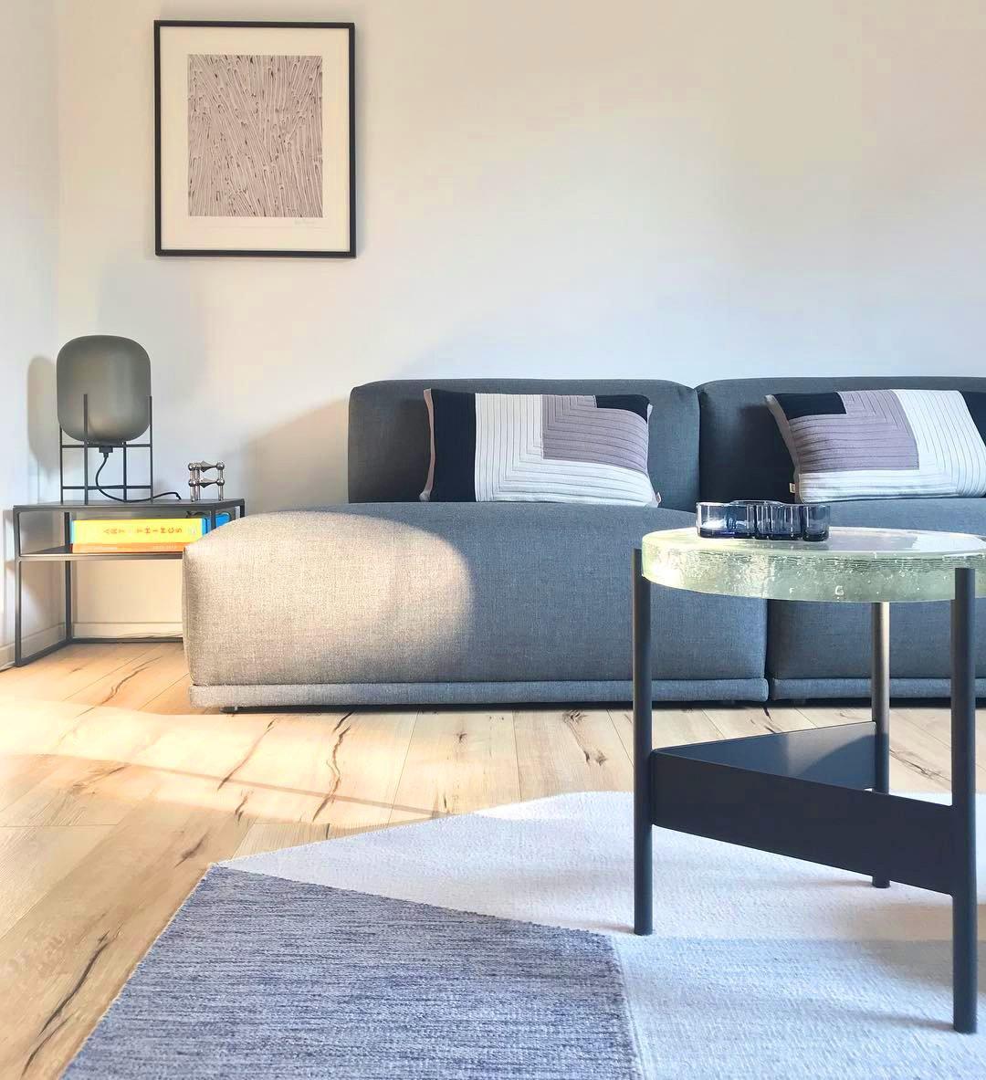 Smoky glass Clérachic table lamp at the far end of a sofa in a bright living room with a pale rug and a low marble table.
