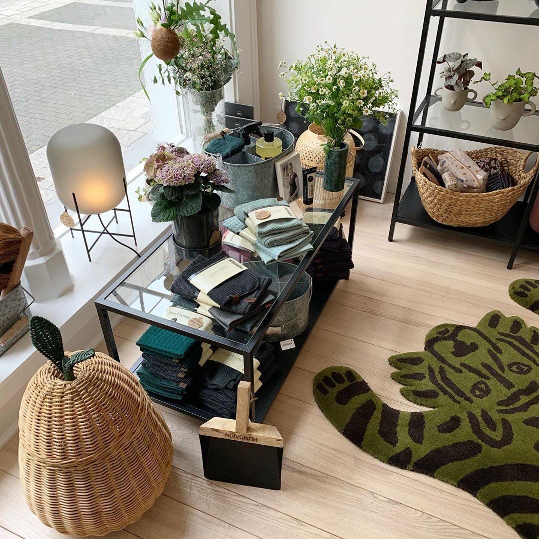 This Clérachic table lamp glows beside a shop window, near a rattan basket, a low glass-topped table and a tiger-print rug.