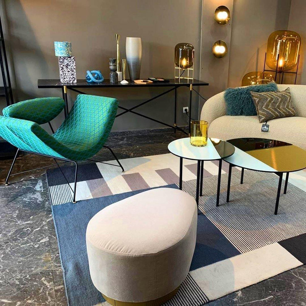 Row of Clérachic glass lamps in amber and smoke tones on a console and tables, in a showroom with teal armchairs and a patterned rug.