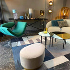Row of Clérachic glass lamps in amber and smoke tones on a console and tables, in a showroom with teal armchairs and a patterned rug.