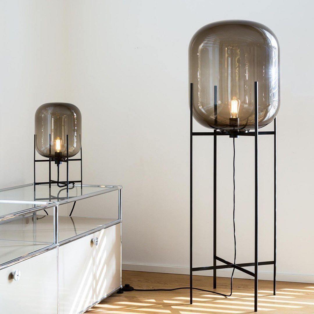Short and tall glass lamps from Clérachic side by side, the tall one on a floor stand beside a white glass cabinet.