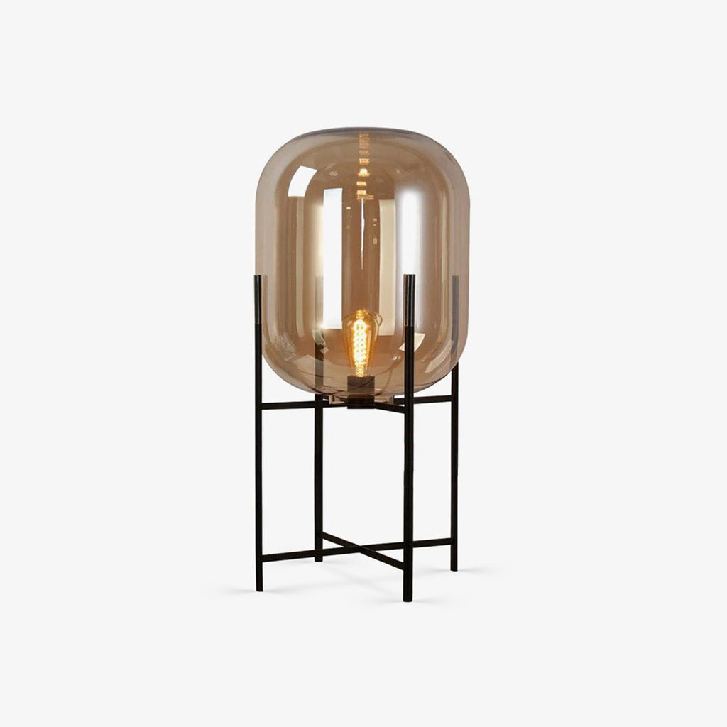 Amber glass shade with a visible filament bulb on a slim black four-leg stand, this Clérachic lamp on a plain light grey background.